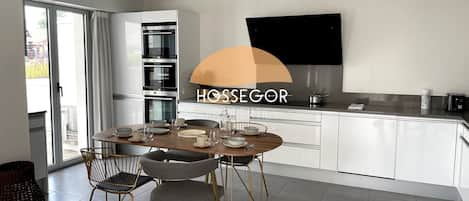 A modern kitchen with a dining area, built-in ovens, and a flat-screen TV.