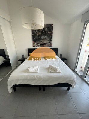 Ein modernes Schlafzimmer mit einem großen Bett, einer hängenden Leuchte, einem Stadtbildgemälde und Blick durch eine Glastür.