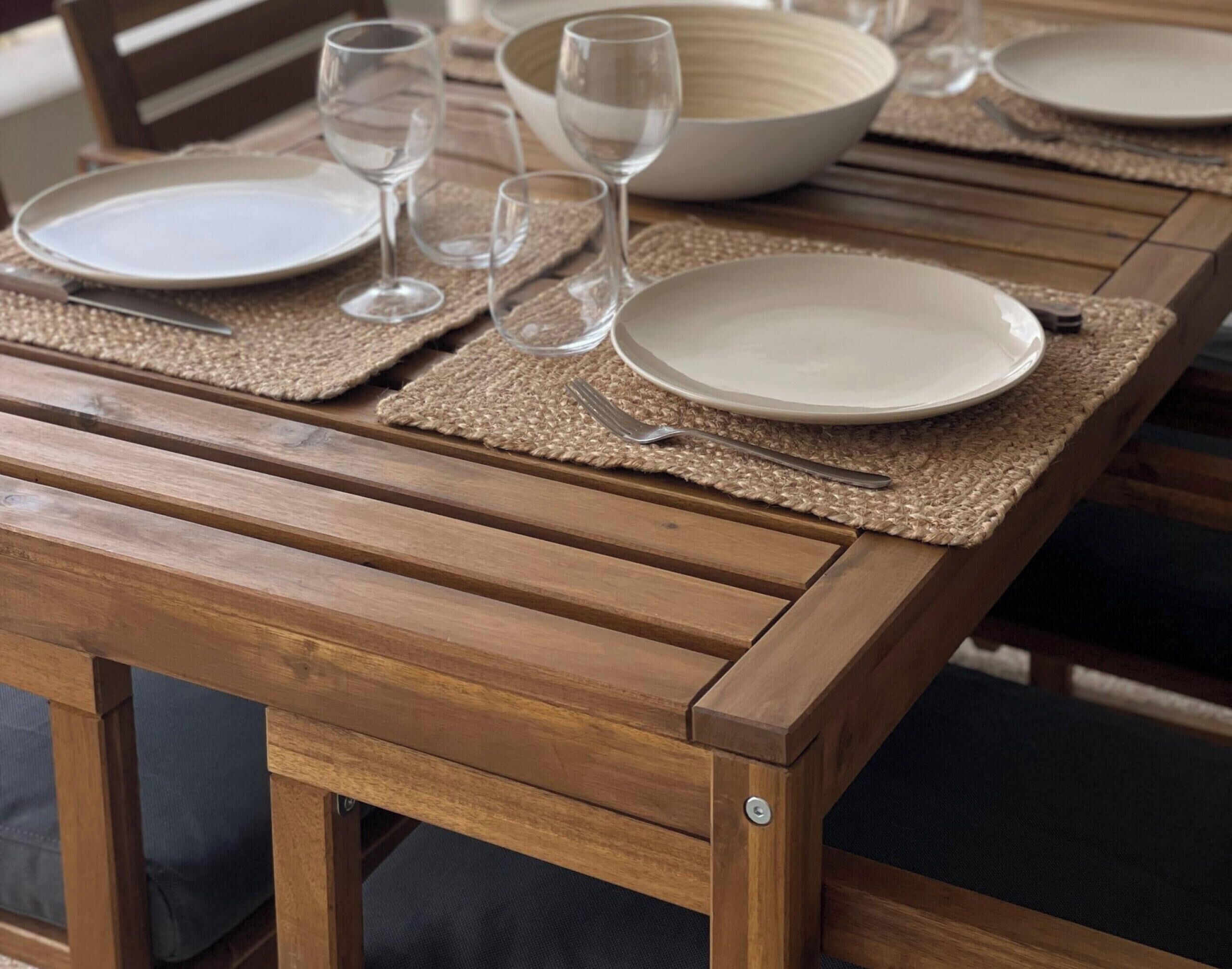 A wooden dining table with placemats, plates, and cutlery.