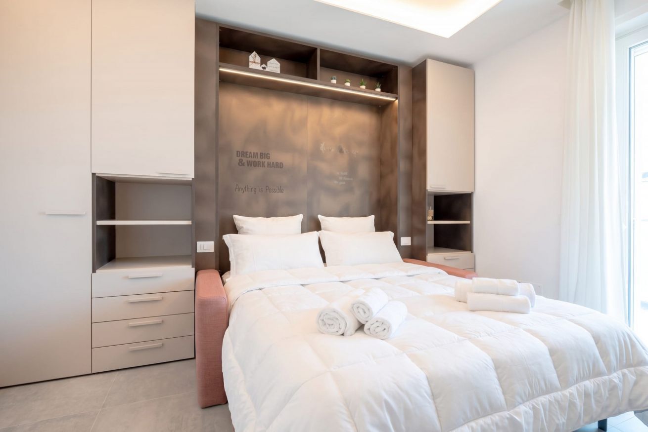 Una camera da letto moderna con un letto grande, spazio contenitivo integrato e una frase motivazionale sulla testiera.