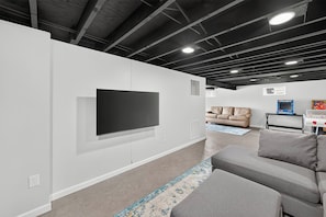 A modern living room with a flat-screen TV mounted on the wall, a grey sofa, and a patterned rug. - Family Friendly STL Area Retreat with Game Room (Fenton)