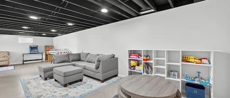 A modern living room with a sectional sofa, a small round table, and a bookshelf filled with children's toys.