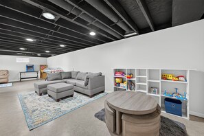 Un saló modern amb un sofà modular, una taula rodona petita i una prestatgeria plena de joguets infantils.