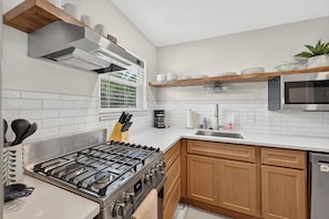 A modern kitchen with a gas stove, stainless steel appliances, wooden cabinets, and a window with blinds. - Family Friendly STL Area Retreat with Game Room (Fenton)