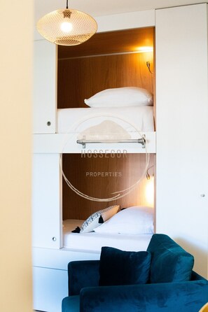 Ein kleines Zimmer mit einem Etagenbett, einer Pendelleuchte und einer Schlafcouch.
