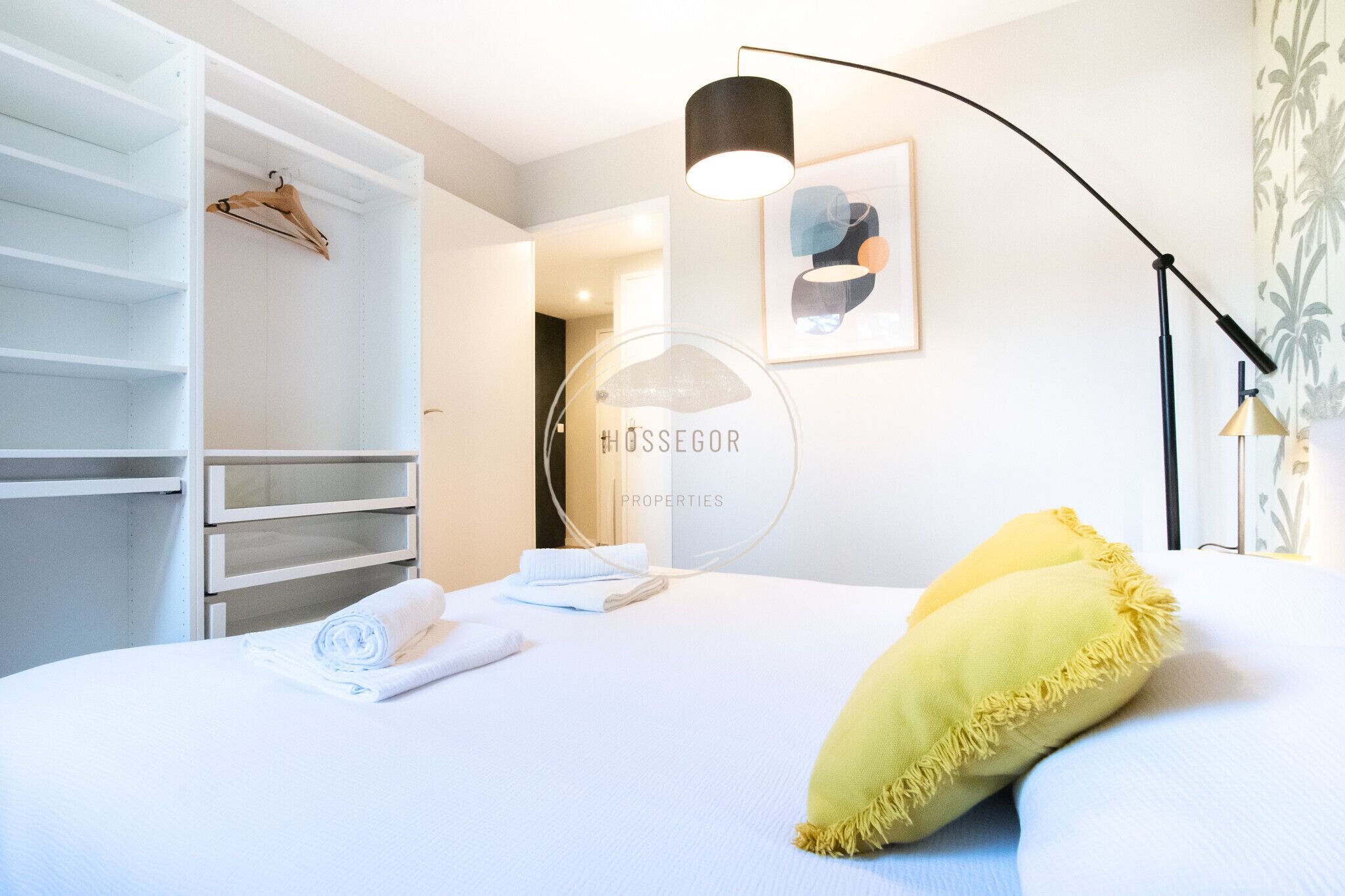 A hotel room with a bed, a wardrobe, a framed picture, and a lamp.
