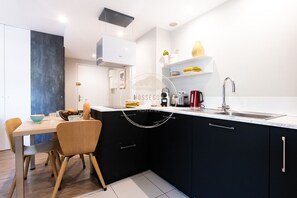 A modern kitchen with a dining area, featuring a black countertop, white cabinets, and a stainless steel sink.