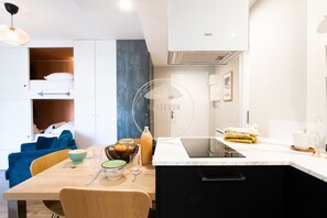 Eine moderne Küche mit Backofen, eine Essecke mit Tisch für zwei Personen und ein blaues Sofa im Hintergrund.