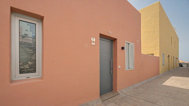 Um edifício com porta cinza, janela e fachada de pedra, além de uma parede amarela.