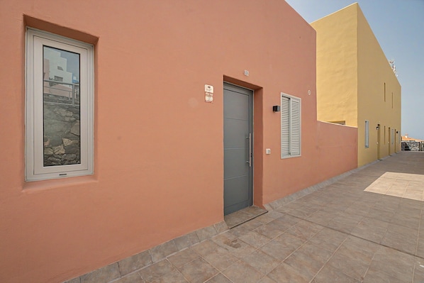 A building with a grey door, a window with a stone facade, and a yellow wall.