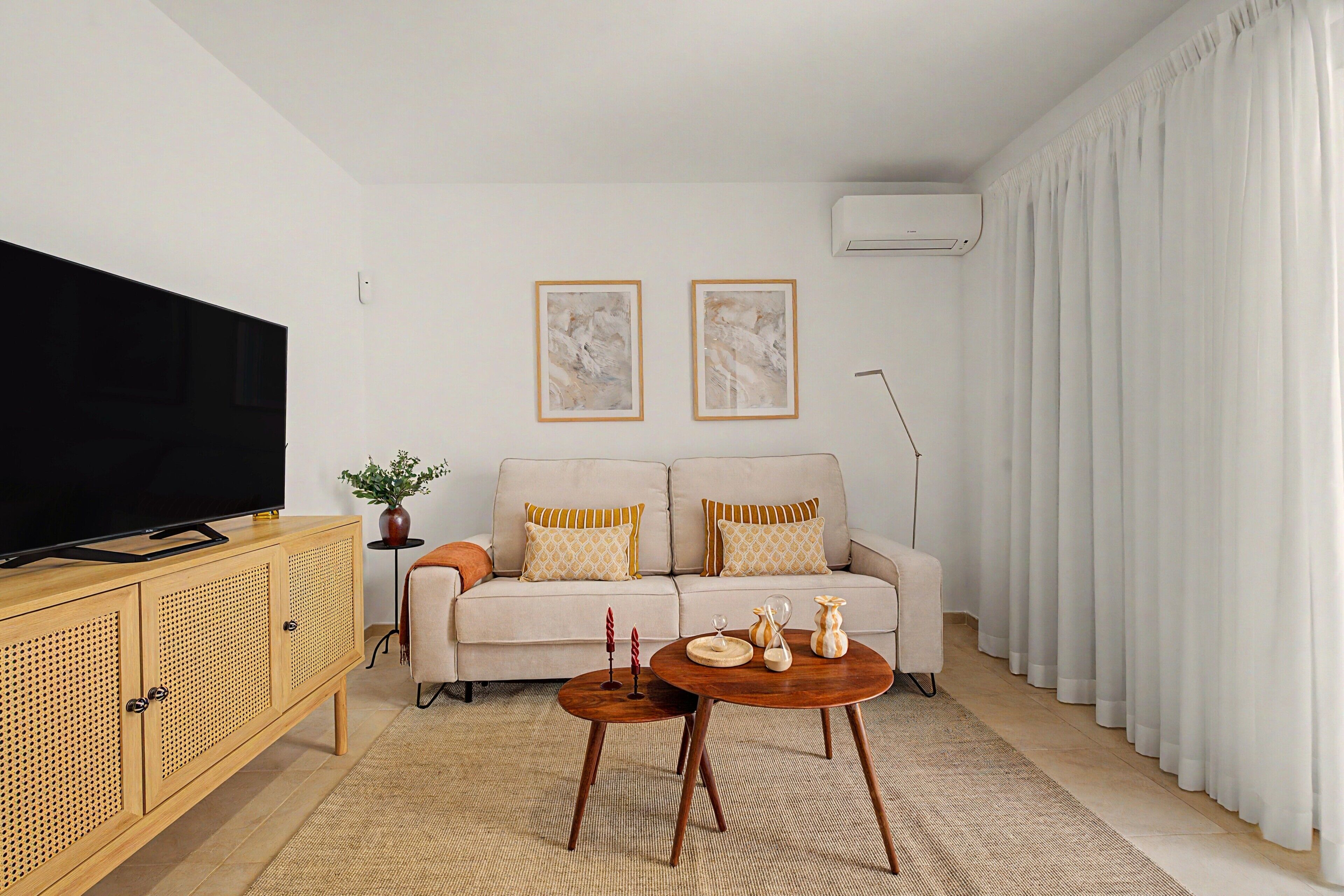 Una sala de estar con televisor de pantalla plana, un sofá con cojines, una mesa de centro y un jarrón decorativo.