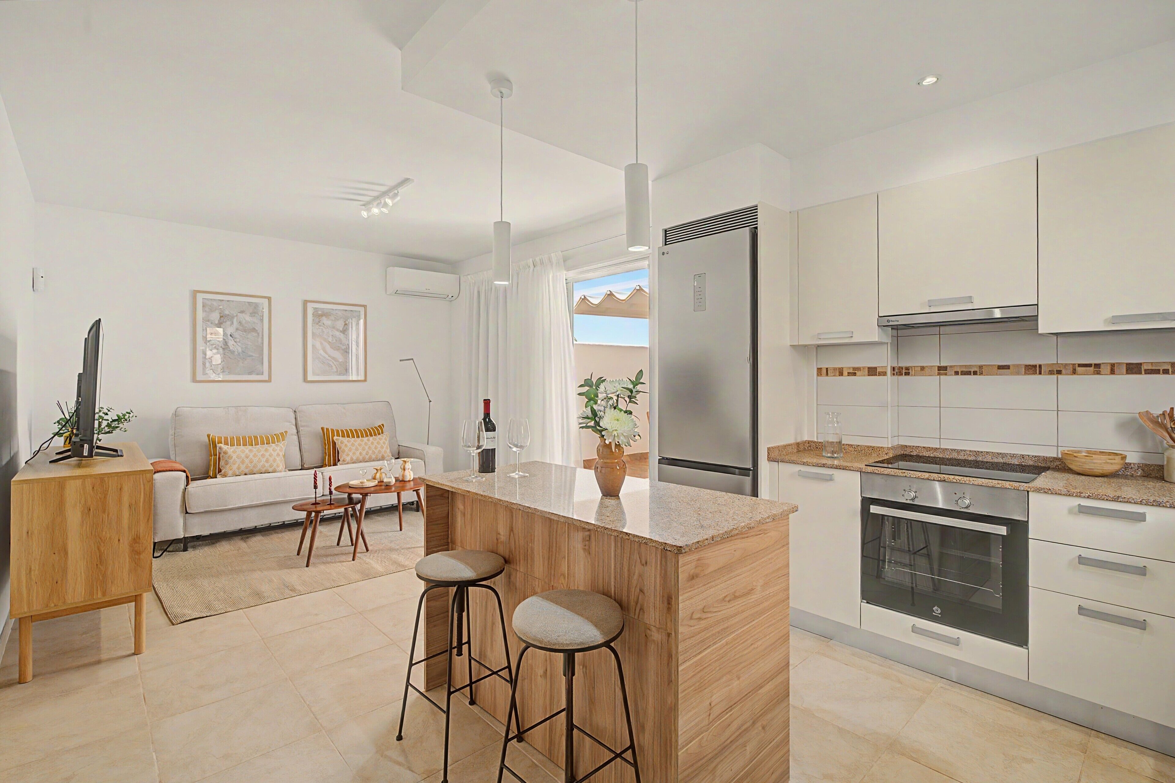 Et moderne køkken med en central ø, rustfrit stål hvidevarer og et spiseområde med en sofa og barstole.