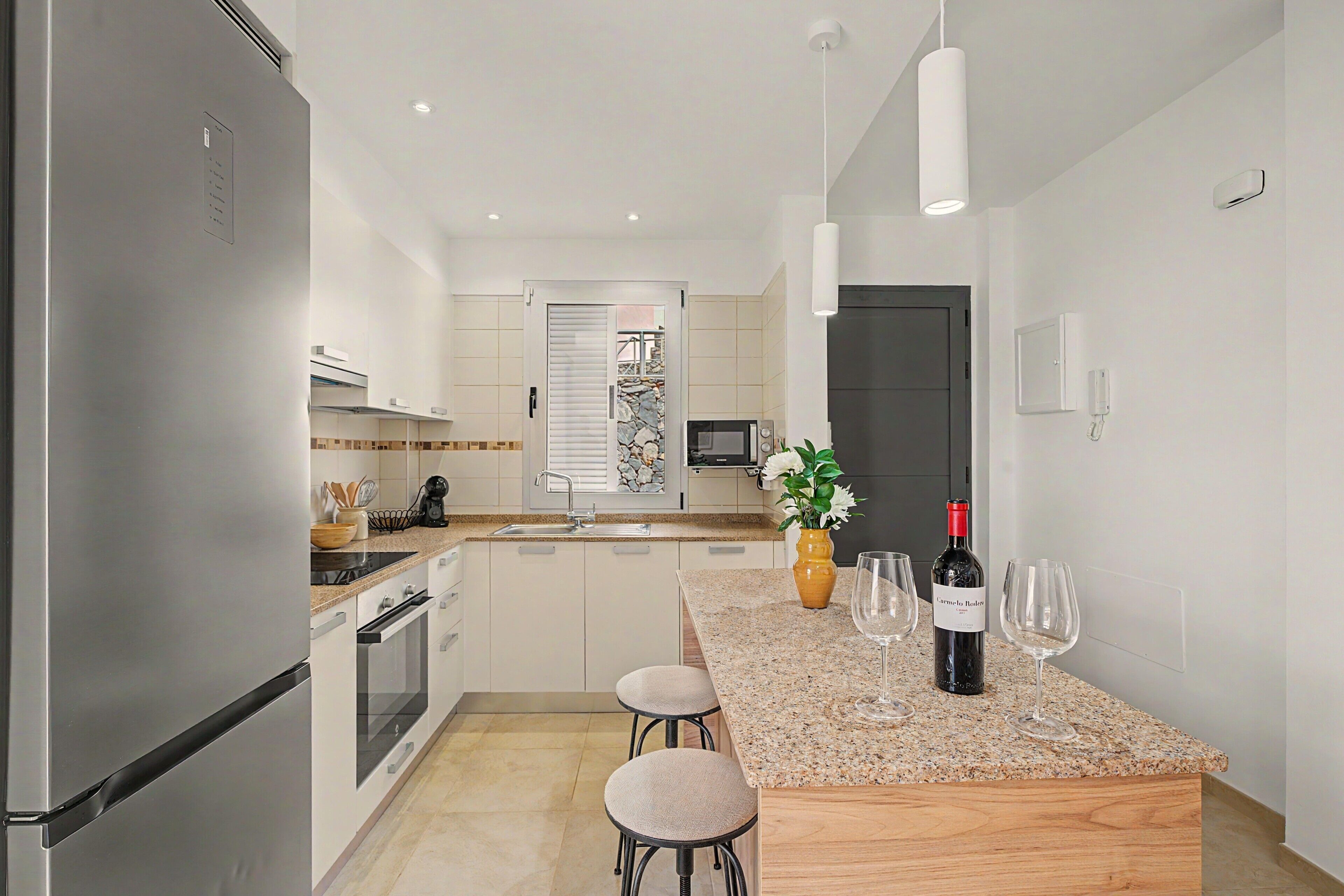 Cocina moderna con encimera de granito, electrodomésticos de acero inoxidable y una isla central con taburetes de bar.