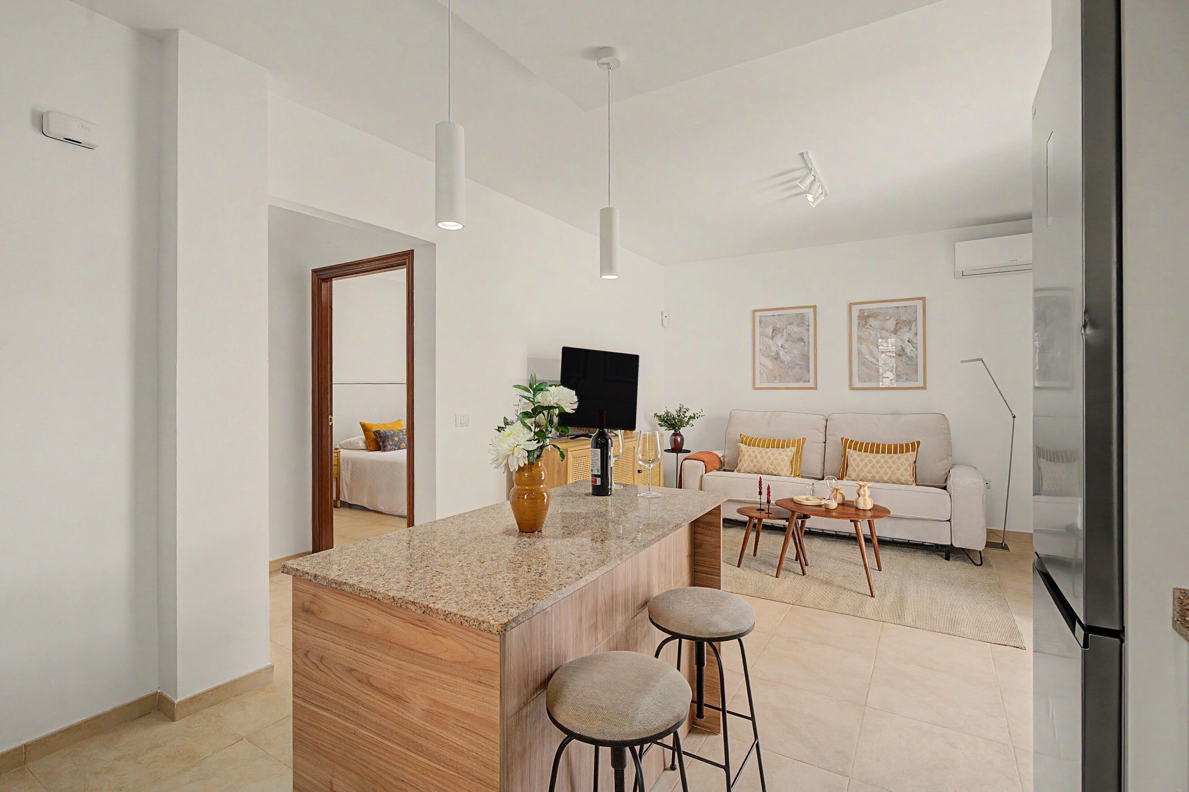 Una cocina moderna con una isla central, taburetes de bar, un televisor de pantalla plana y un sofá al fondo.