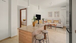 Cozinha moderna com ilha central, banquetas, televisão de tela plana e um sofá ao fundo.