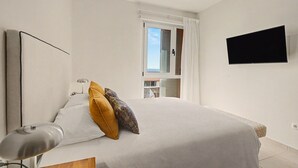 Quarto com cama, luminária de mesa, televisão de tela plana e janela com persianas.