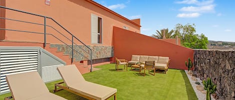 Un patio con dos sillones de descanso, un muro de piedra y una escalera que conduce a un segundo piso.