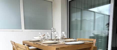 A dining table set with plates, glasses, and a pitcher, positioned in a room with large windows and a view of the outside.