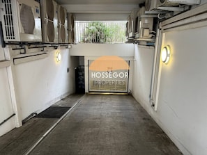 A hallway with air conditioning units on the walls, a metal gate, and a sign reading 'HOSSEGOR PROPERTY'. - Appt Brémontier 3 - Hossegor center - Terrace (Soorts-Hossegor)