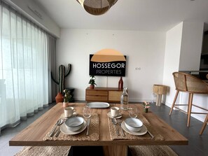 A dining area with a wooden table set for four, a cactus decoration, and a wall sign for 'HOSSEGOR PROPERTIES'. - Appt Brémontier 3 - Hossegor center - Terrace (Soorts-Hossegor)