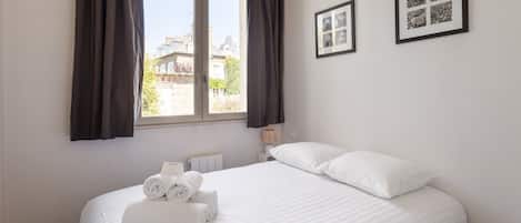 Habitación de hotel con una cama grande, dos cuadros en la pared, una ventana con cortinas y un radiador.
