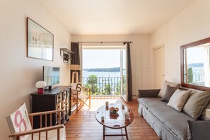 Una habitación con balcón, sofá, mesa de centro, televisor y un cuadro en la pared.