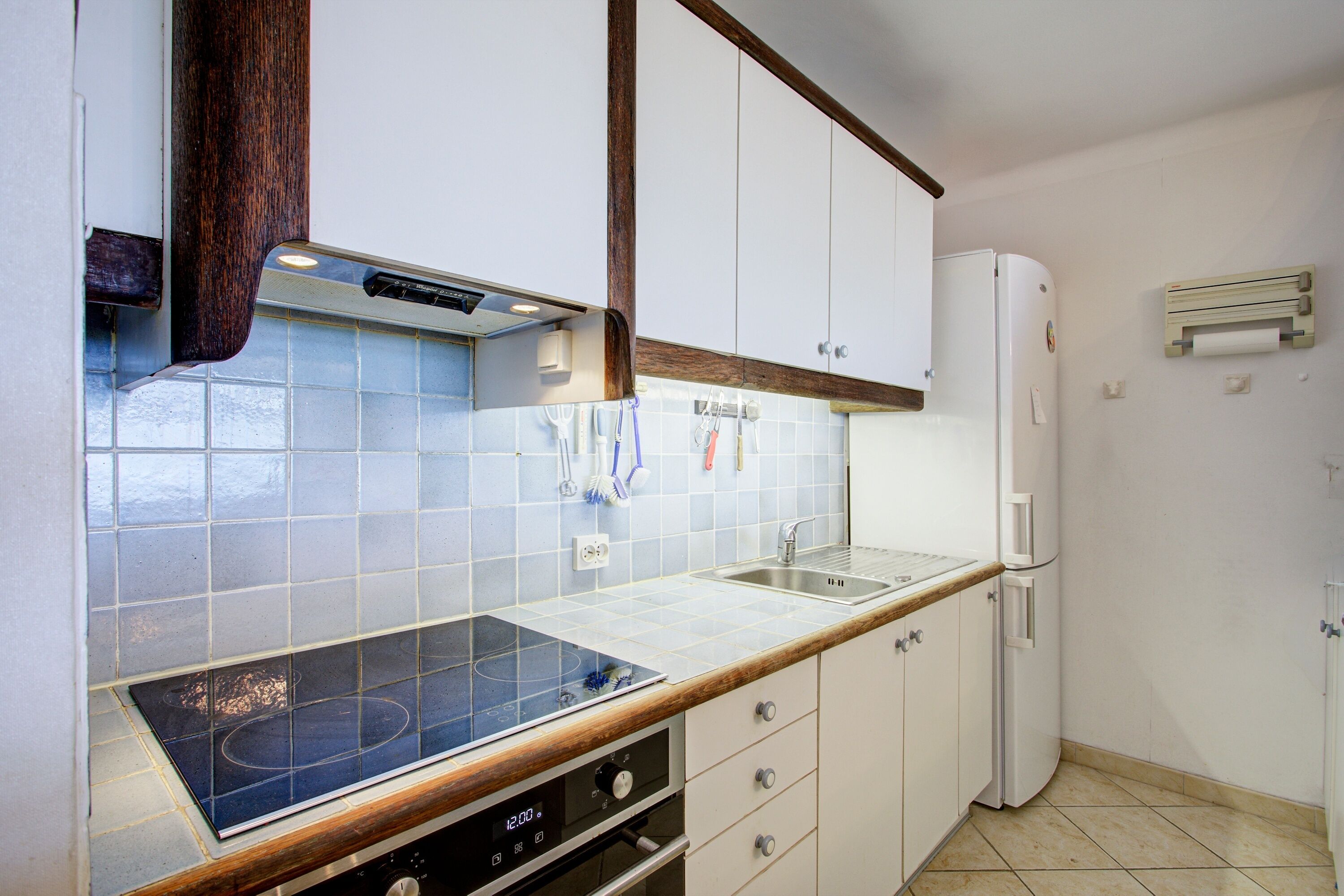 A kitchen with a stove, sink, cabinets, and a refrigerator.