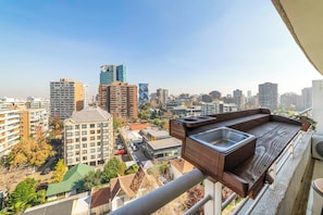 A balcony with a wooden table and a sink, overlooking a cityscape with various buildings and a clear sky. - Trendy Apartment Las Condes | Modern City Living (Santiago)