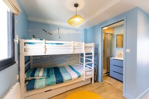 Een stapelbed met een muurschildering van een meeuw, een badkamer met een glazen douche en een geel vloerkleed.