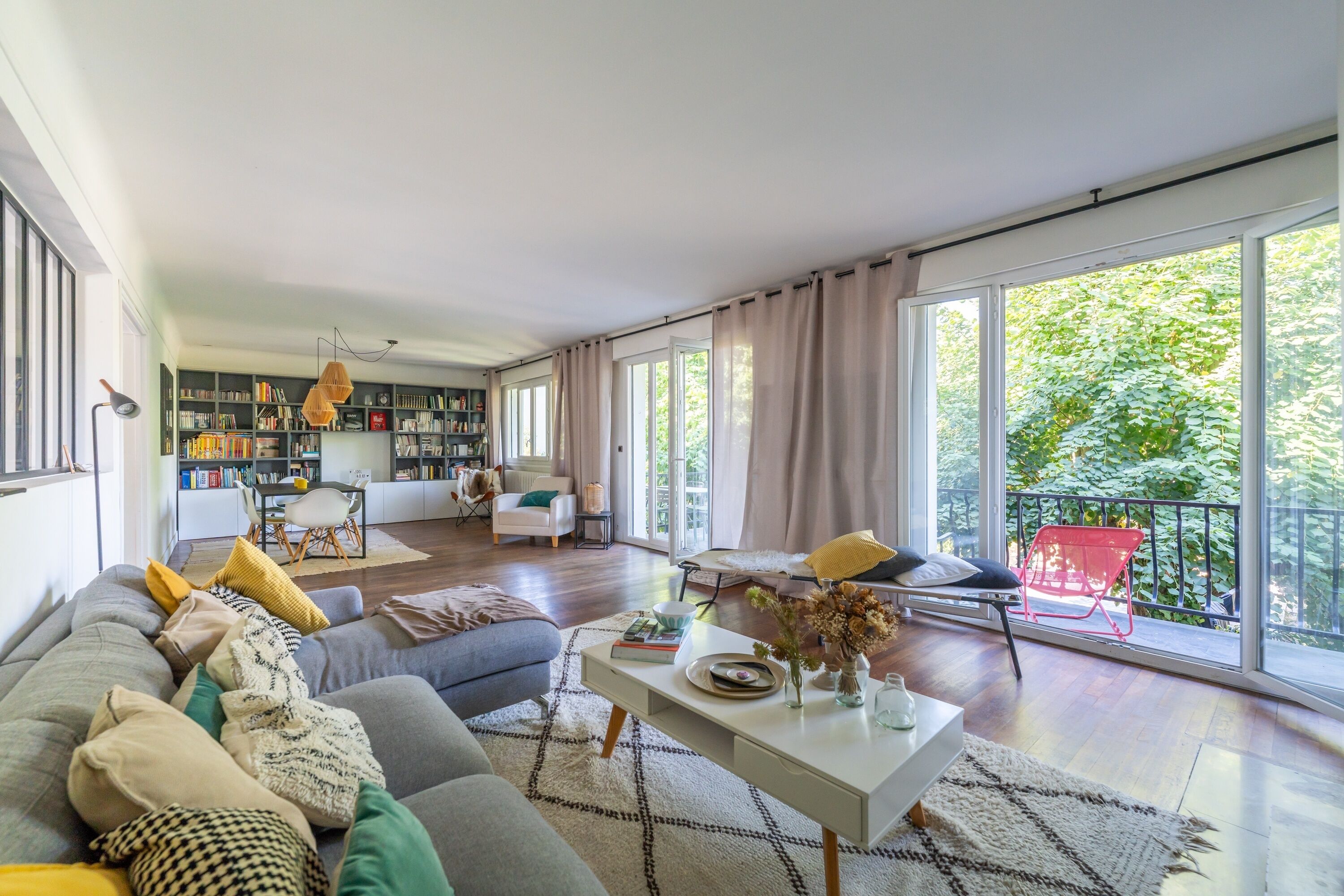A spacious living room with a large sofa, a dining area, and a bookshelf.