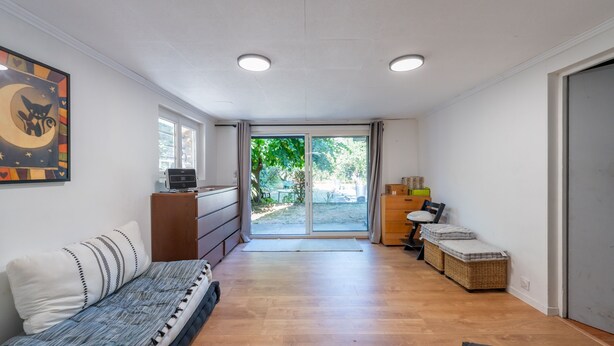 Ein Zimmer mit einer Sitzecke, einem kleinen Tisch, einem Schrank und einem Fenster mit Blick auf Grünflächen.