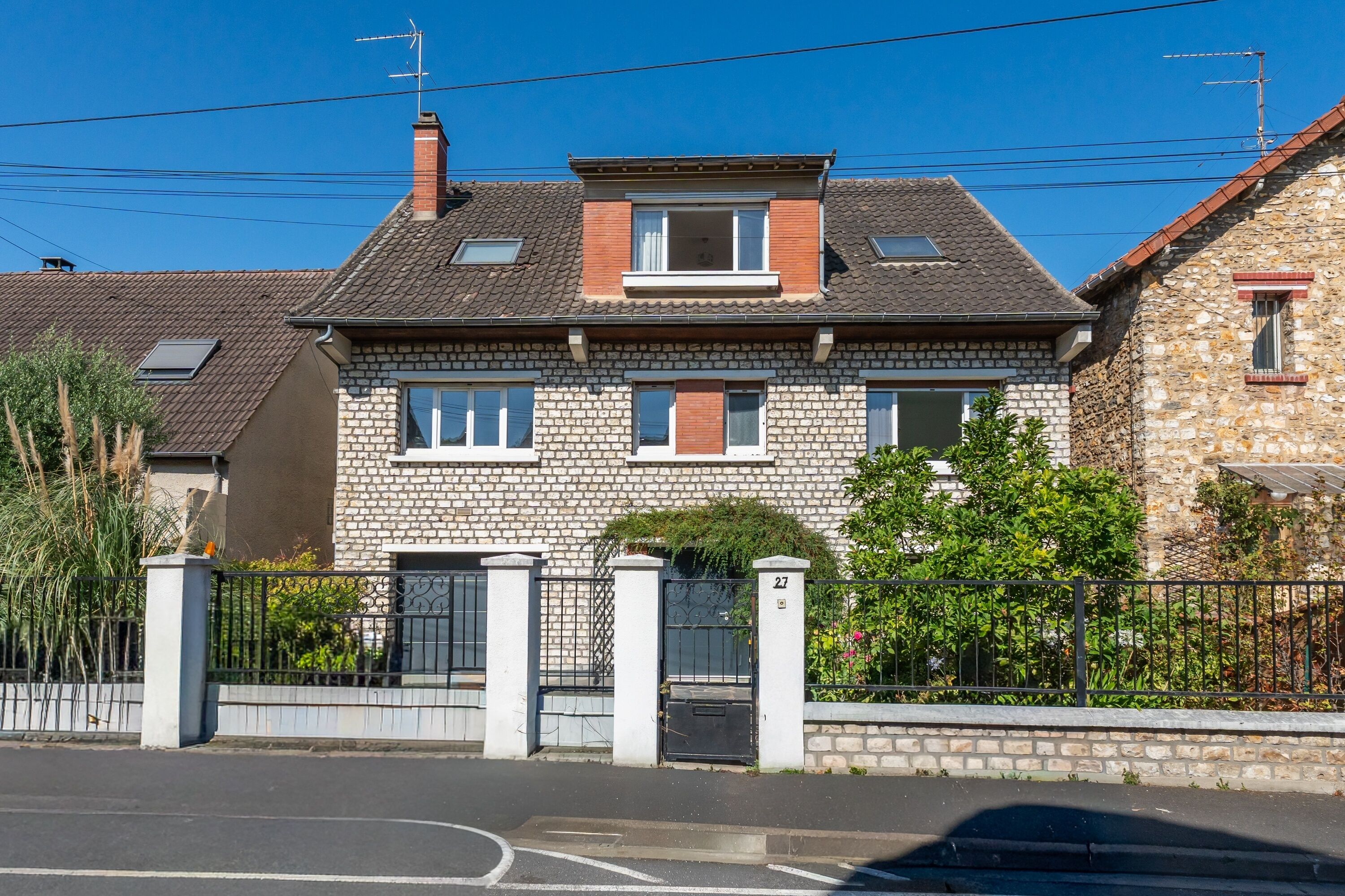 A two-story house with a stone facade, a tiled roof, and a gated entrance.