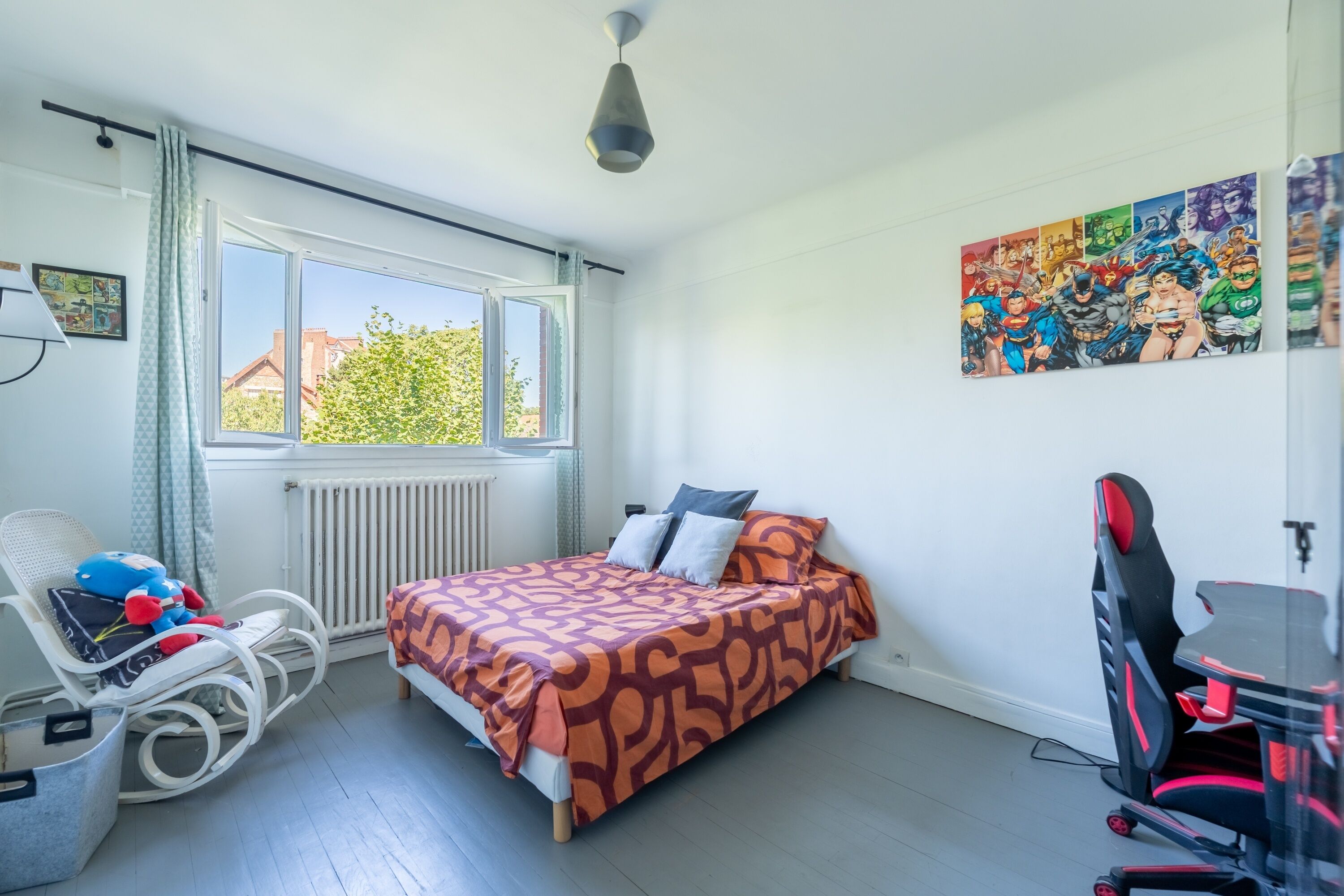 Ein Schlafzimmer mit Bett, Sessel, Schreibtisch und Fenster.