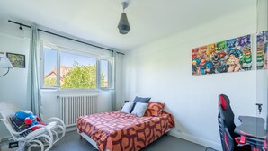 Ein Schlafzimmer mit Bett, Sessel, Schreibtisch und Fenster.
