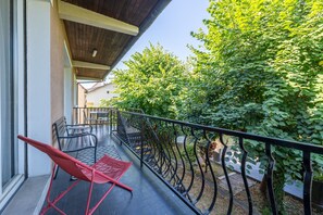Ein Balkon mit rotem Stuhl, Metallgeländer und Blick auf einen Garten mit Bäumen.