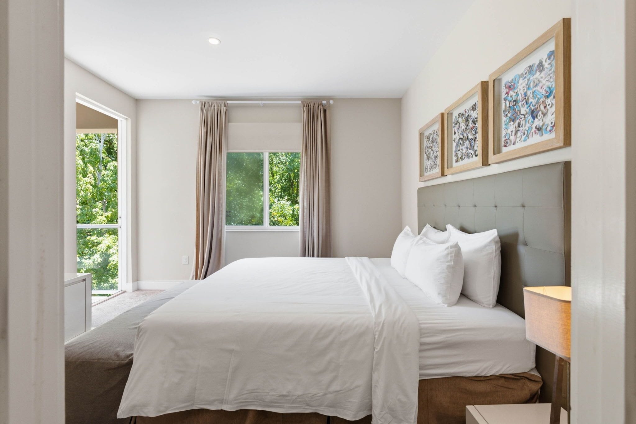 Ein Schlafzimmer mit einem großen Bett, einem Fenster mit Vorhängen und gerahmten Kunstwerken an der Wand.