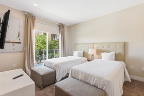 Ein Hotelzimmer mit zwei Betten, einem Fernseher, einem Schreibtisch und einem fenster mit Vorhängen.