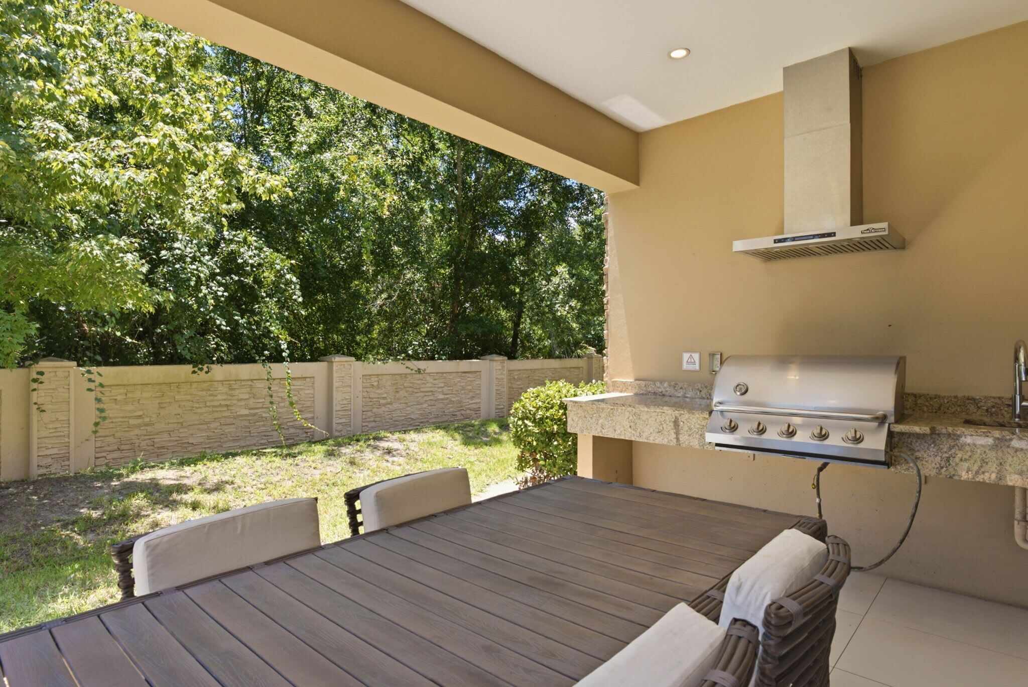 An outdoor patio with a grill, seating, and a view of a wooded area.