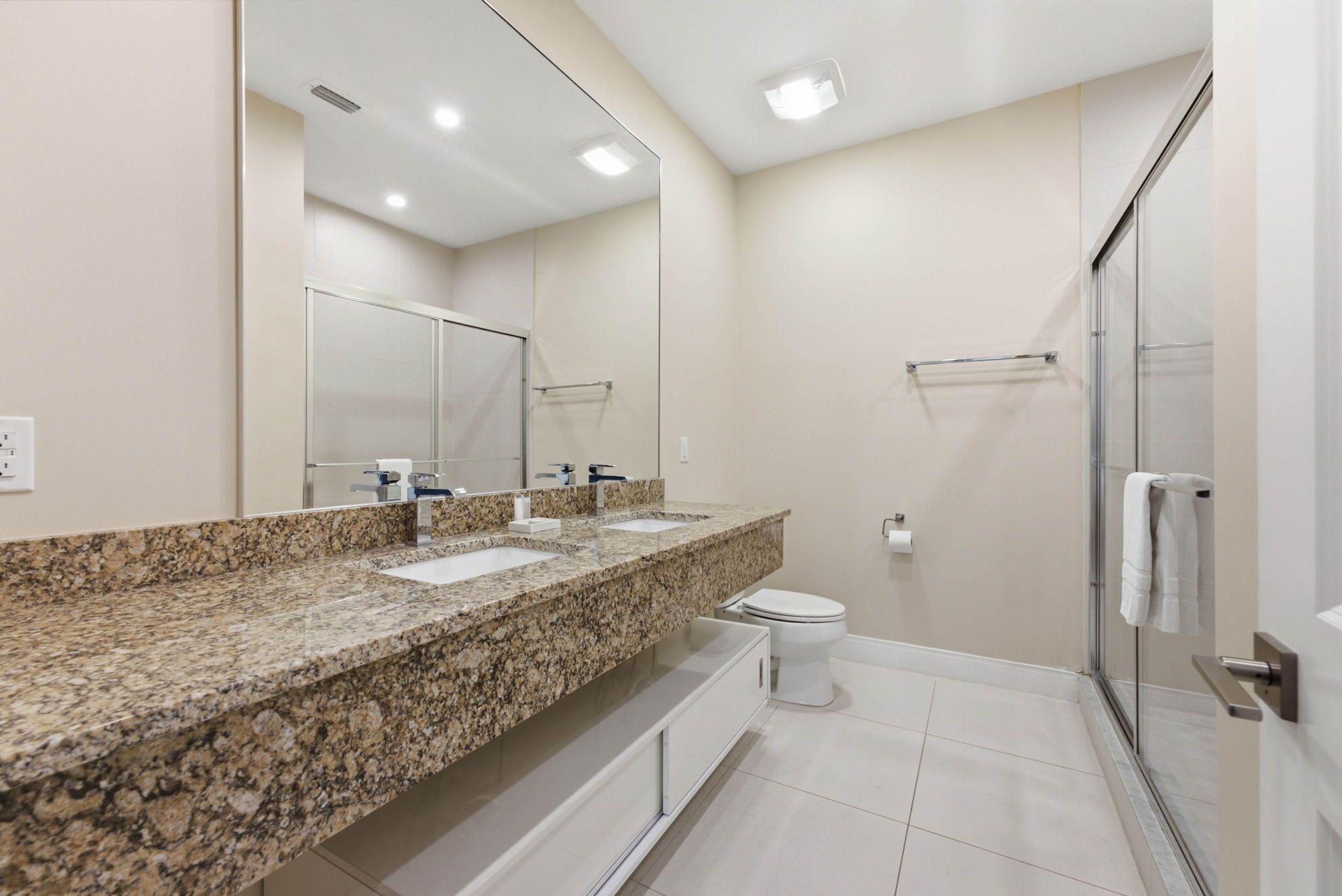 Ein modernes Badezimmer mit einer Granit-Arbeitsplatte, einer Toilette und einer Duschkabine aus Glas.