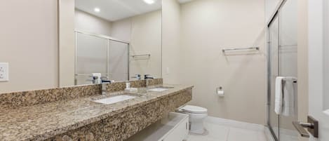 A modern bathroom with a granite countertop, a toilet, and a glass shower enclosure.