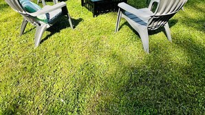Una casa blu con tetto spiovente e un cortile recintato. Nel cortile ci sono quattro poltrone Adirondack e un tavolino.