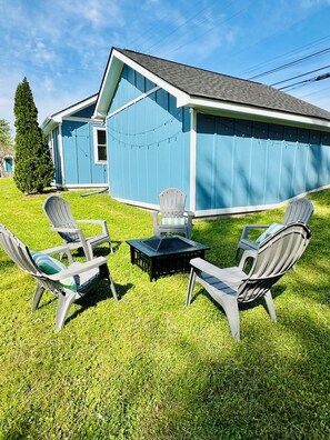 Ein blaues Haus mit einem geneigten Dach und einem eingezäunten Hinterhof. Vier Adirondack-Stühle und ein kleiner Tisch befinden sich im Garten.