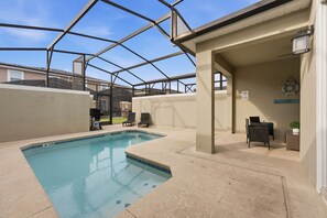 A swimming pool with a glass enclosure, lounge chairs, and a small table with a plant. - Family Friendly Home, Private Pool, Near Disney (Kissimmee)