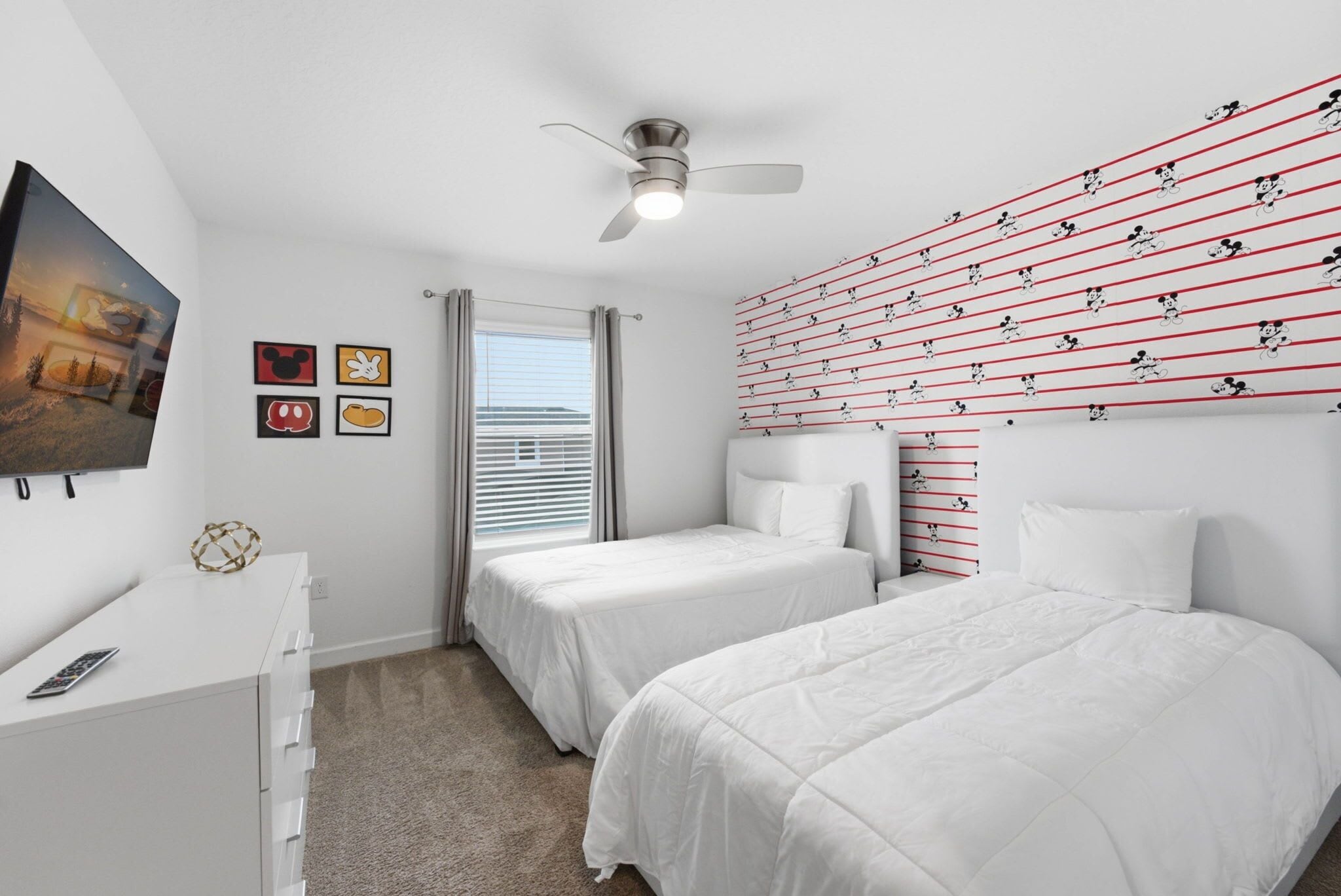 A hotel room with two beds, a ceiling fan, a TV, and a window with curtains.