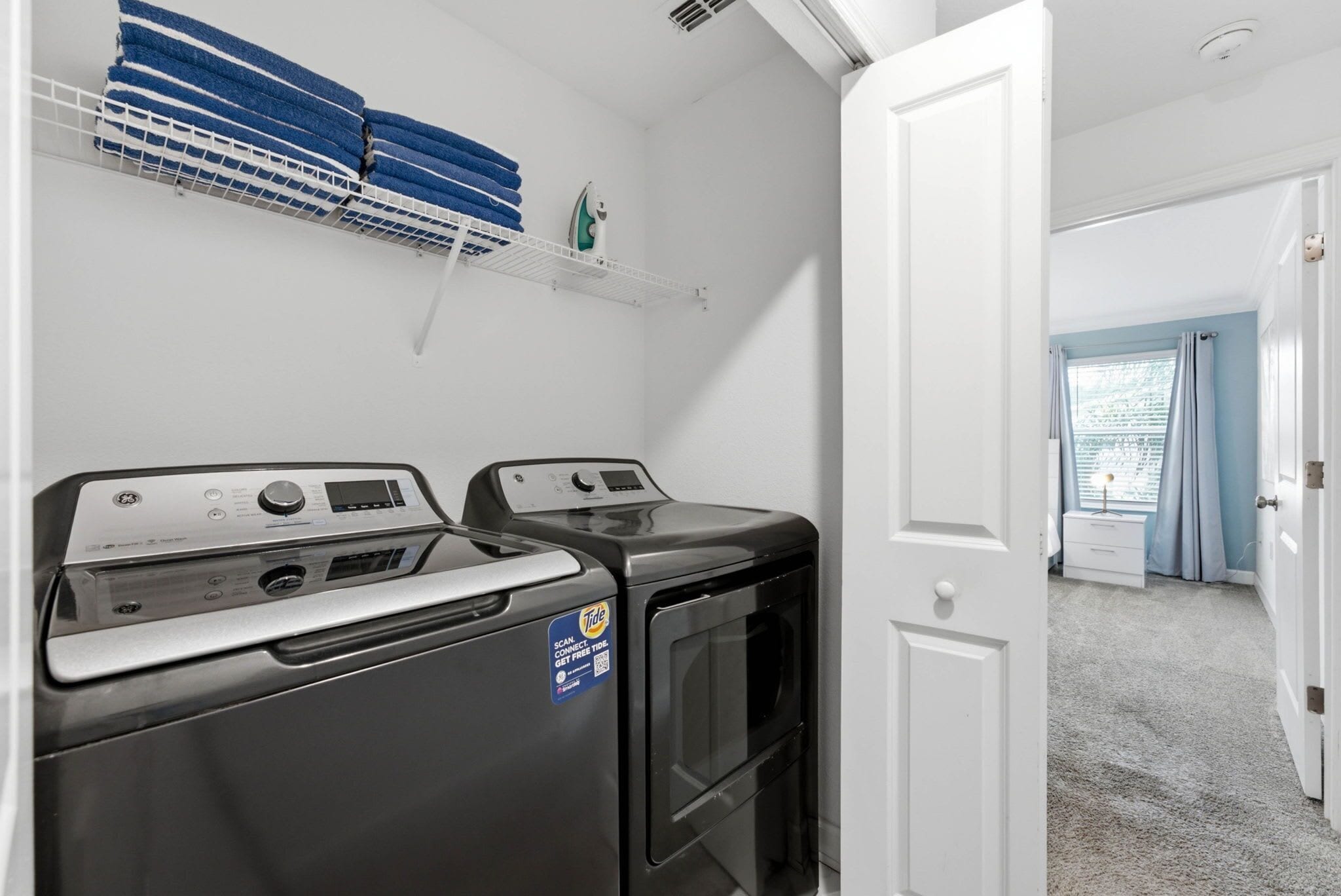 A laundry room with two front-loading washers and dryers, a white door, and a window with curtains.