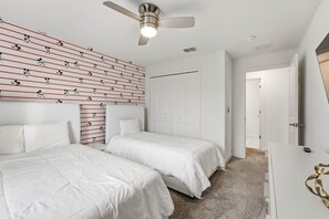 A bedroom with two beds, a ceiling fan, and a wall with a Mickey Mouse pattern.