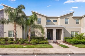A modern two-story residential building with a stone facade, a front entrance with a covered porch, and a well-maintained front yard with palm trees and shrubs. - Family Friendly Home, Private Pool, Near Disney (Kissimmee)