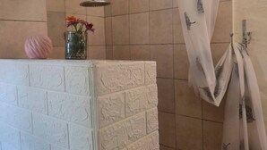 Et bruseområde med en glasvase med blomster, et brusehoved og et håndklædestativ med håndklæder.