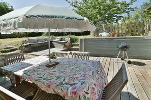Een terras buiten met een tafel, stoelen, een parasol, een barbecue en een tuin.