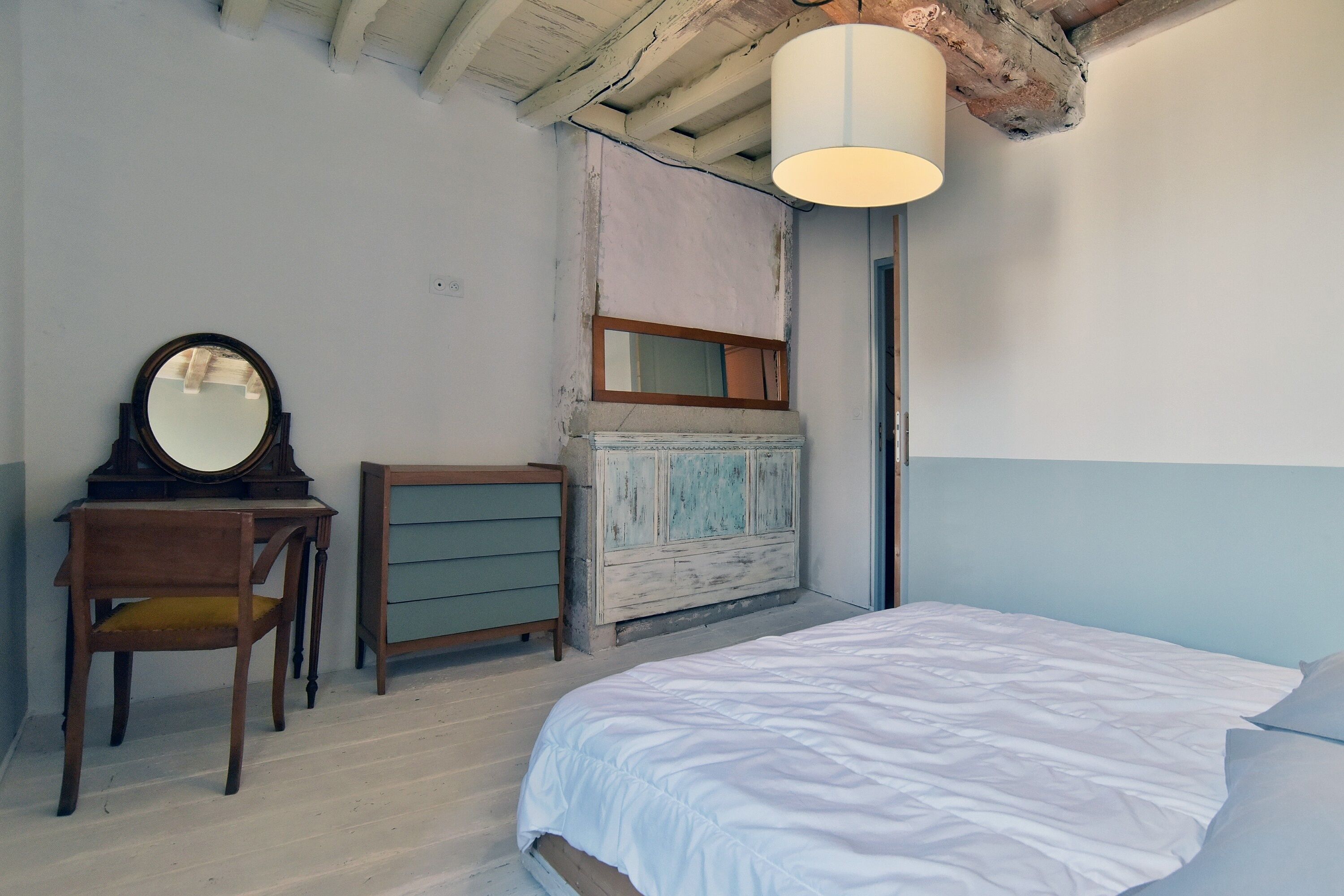 Ein Schlafzimmer mit Bett, Schminktisch, Sessel, Spiegel und Pendelleuchte.